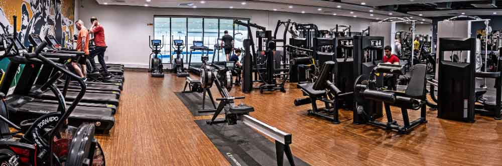 Gym interior with various exercise equipment and people working out.